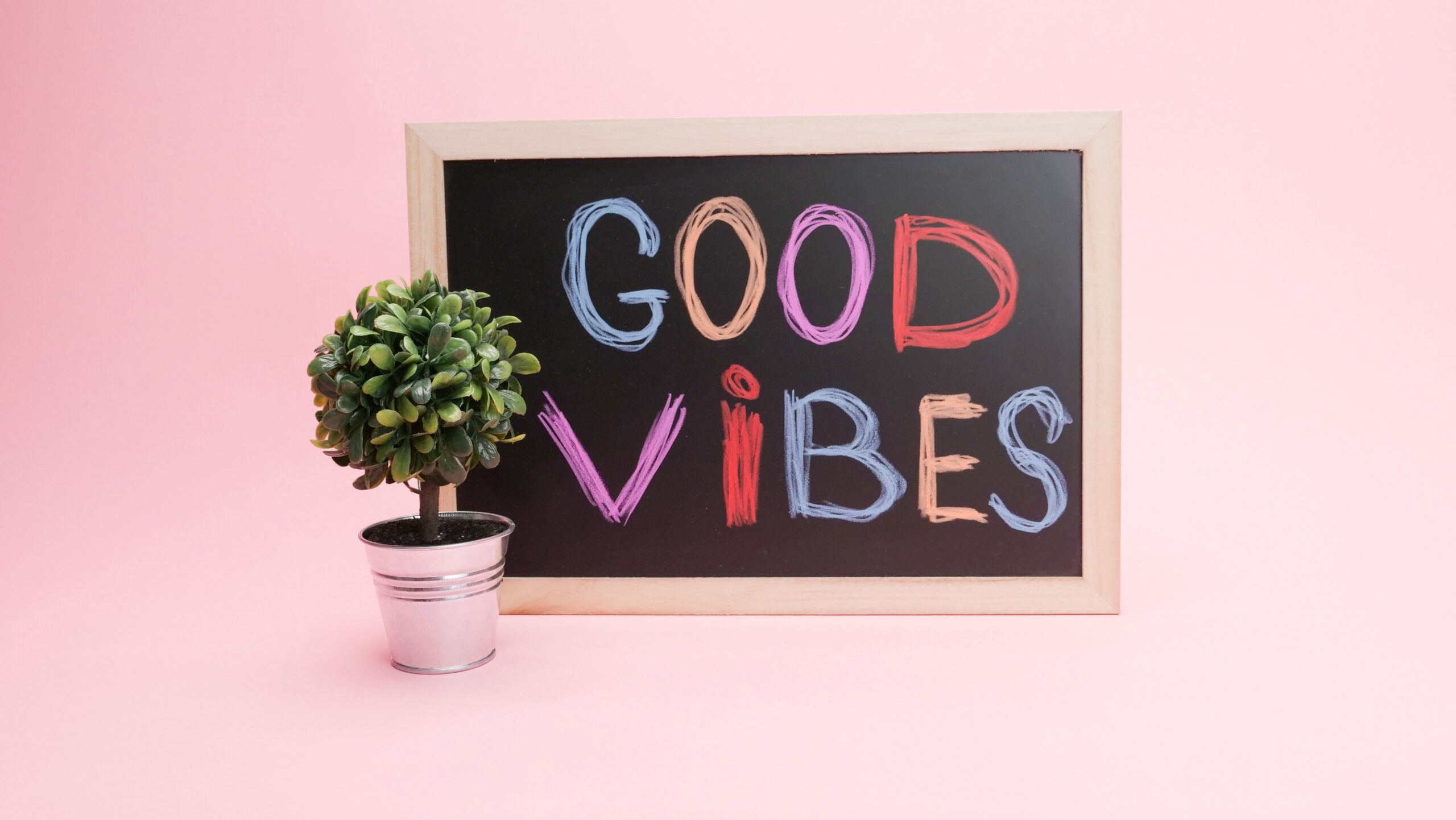 Chalkboard with 'Good Vibes' in colorful letters against a pink background with a potted plant.